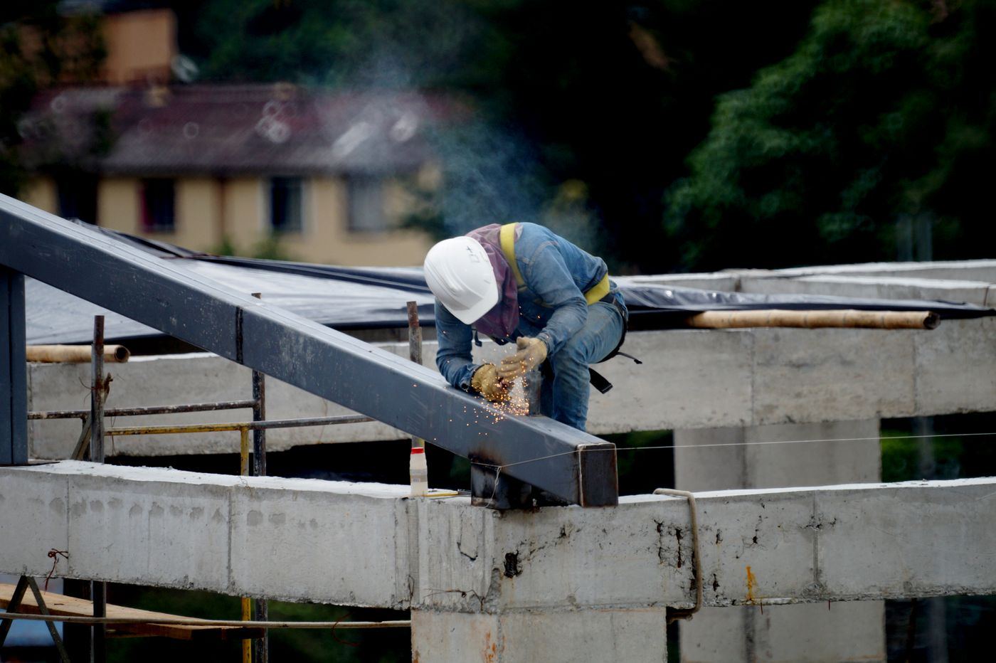 A welder in a hard hat working on a steel rafter above a concrete structure