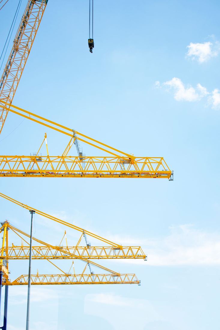 Tower crane jibs and a lifting hook against a pale blue sky
