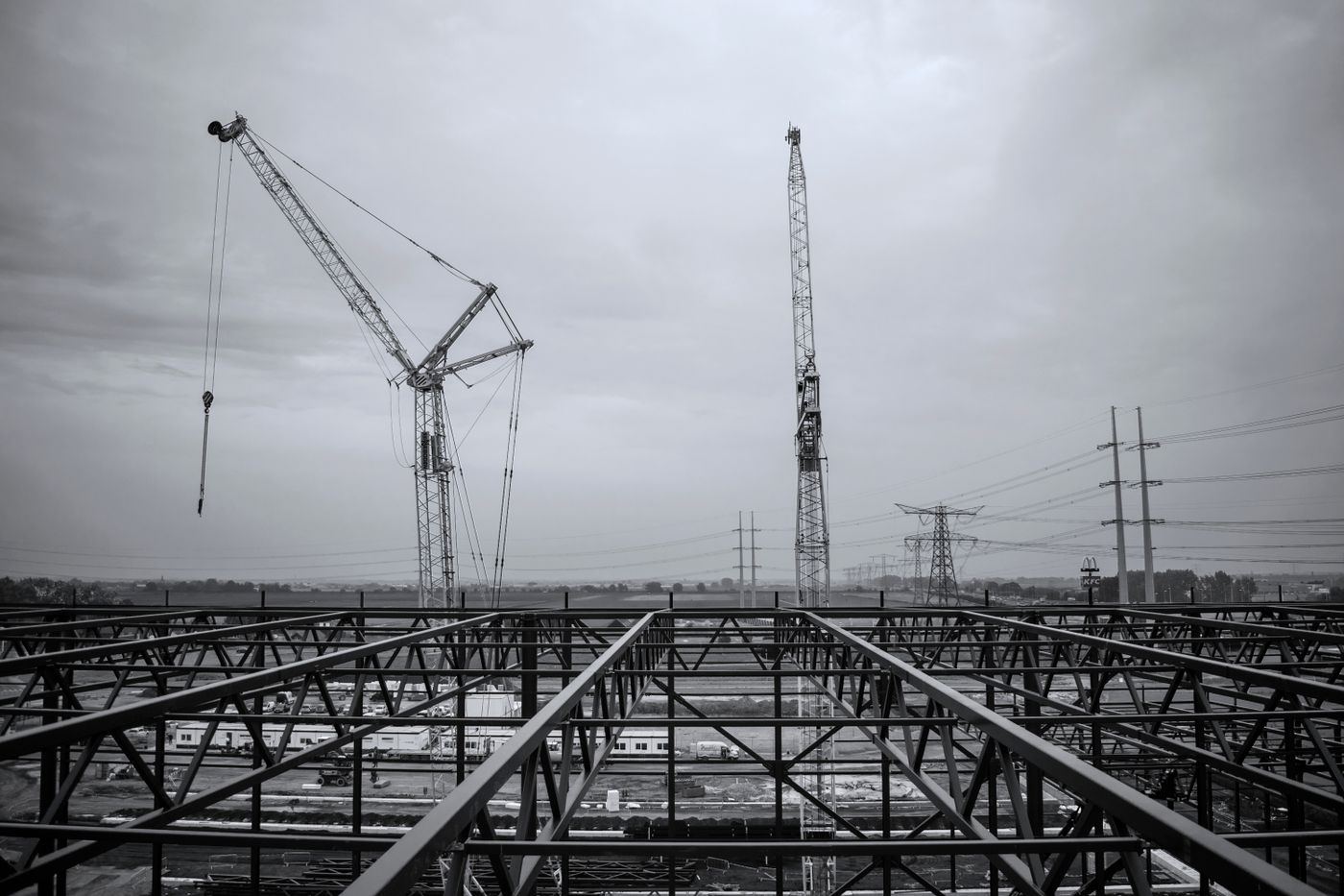 An erected steel roof frame with two cranes standing behind it under a grey sky